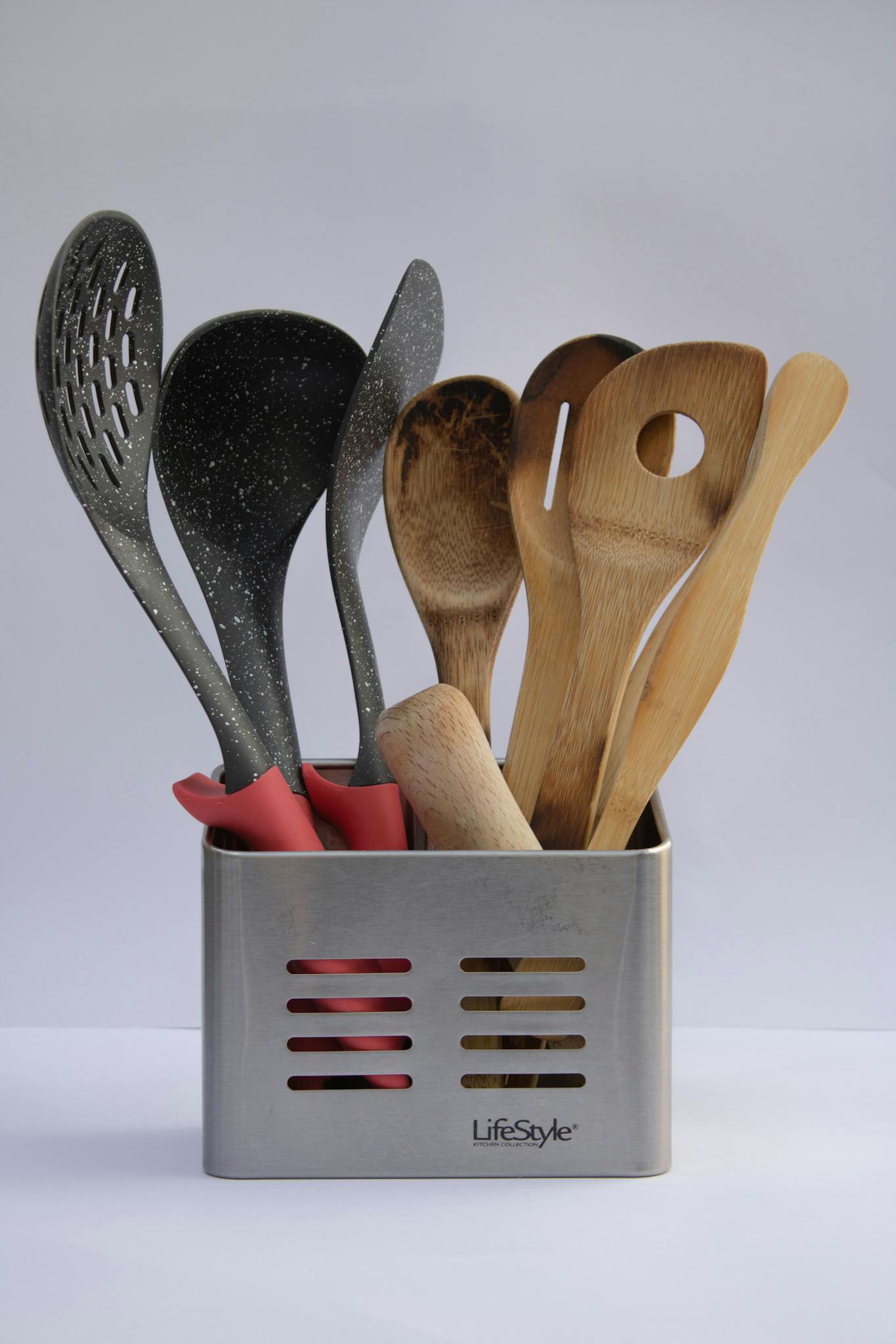 Close-up of assorted kitchen utensils in a stainless steel holder, featuring wooden and plastic spoons.