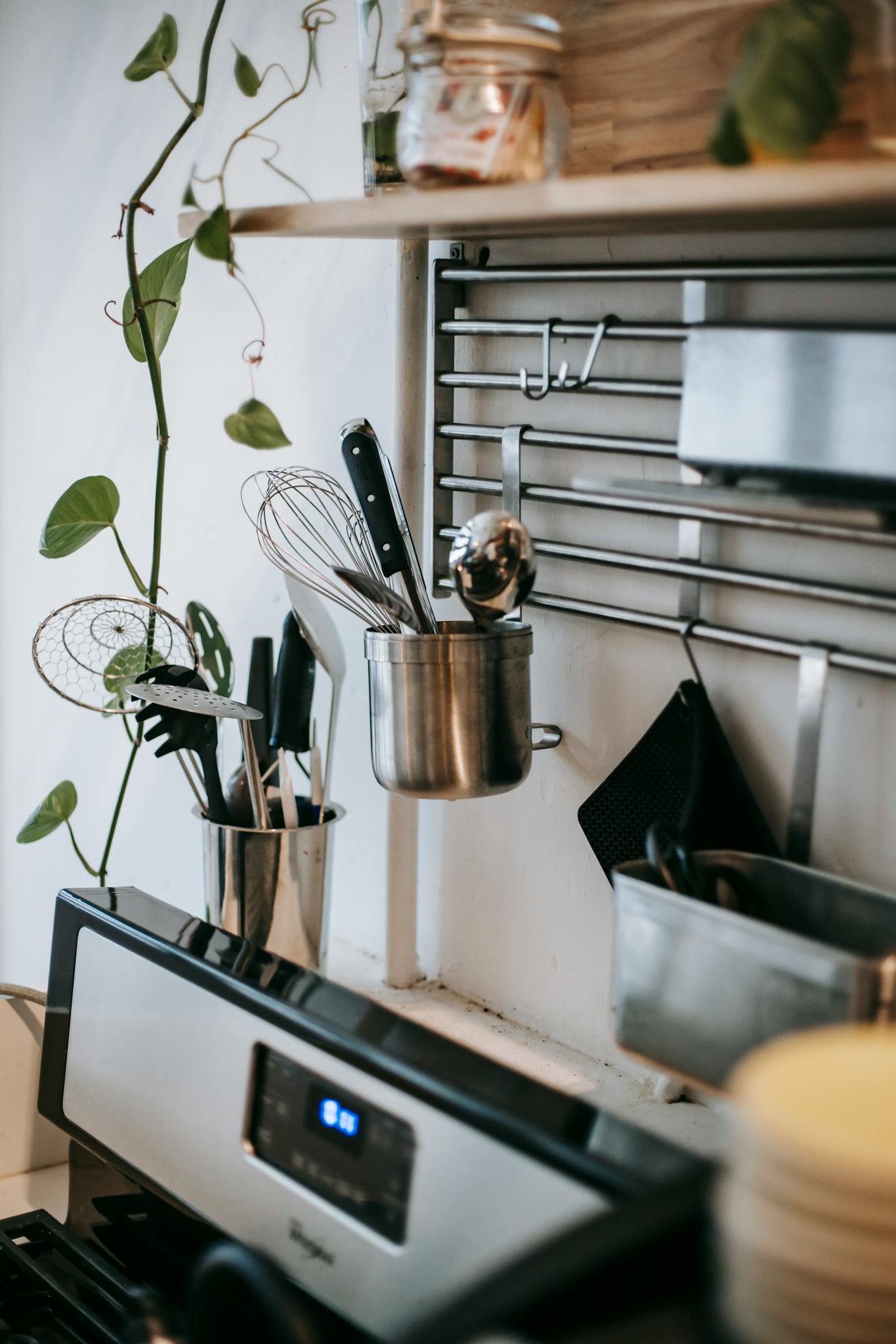 Kitchenware on metal rack with hooks above electric oven with display in house kitchen
